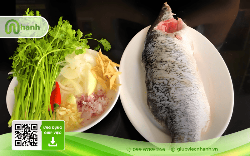 Cá chẽm tươi đã làm sạch đặt cạnh các loại gia vị như hành tây, gừng, tỏi, ớt và rau ngò.